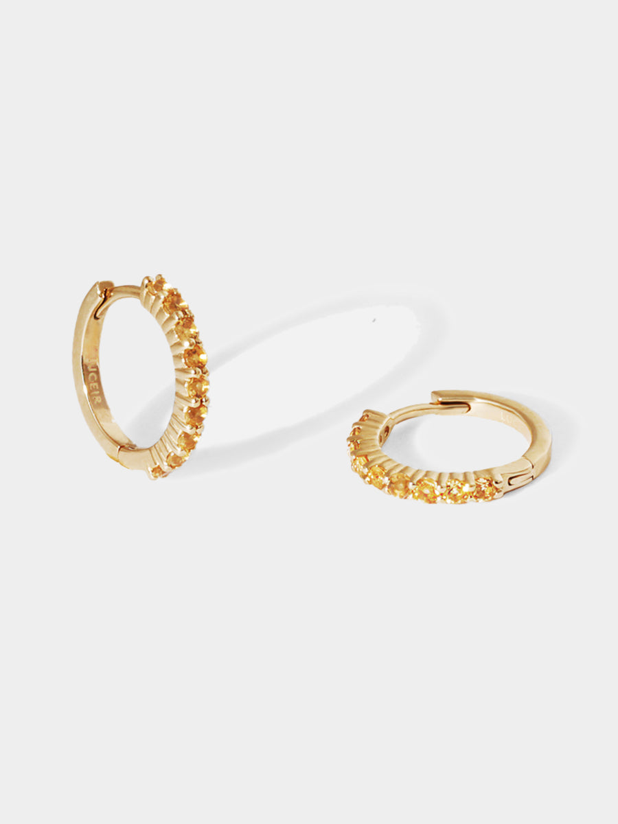 A pair of 9 karat gold huggies with 9 yellow citrine gemstones per huggie. Set on an architectural grey background with elongated huggie shadows