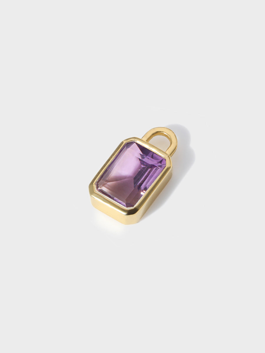 A large Brazilian amethyst baguette shaped charm set in a gold casing with large connection hoop at the top. Grey background with shadow
