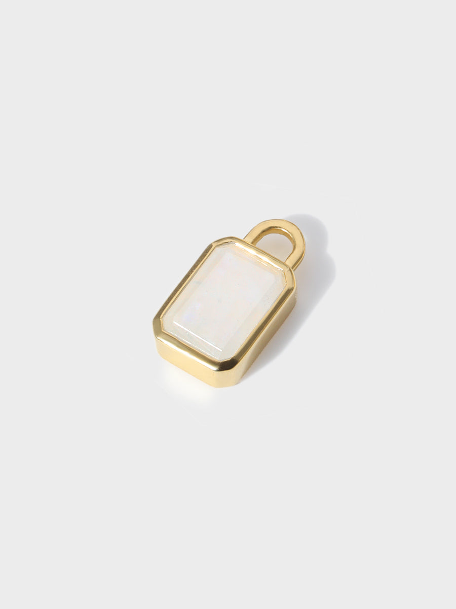 A large moonstone baguette shaped charm set in a gold casing with large connection hoop at the top. Grey background with shadow