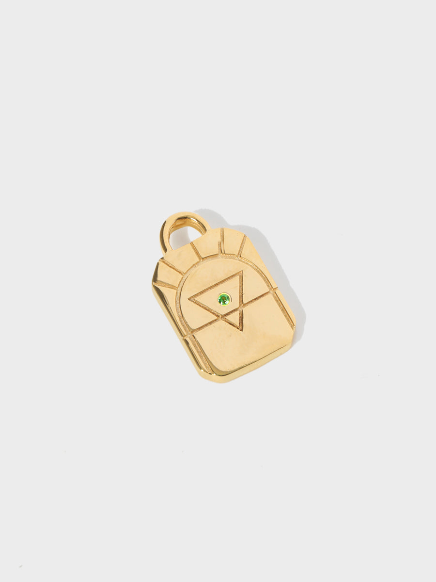 A gold earth element rectangular charm with chamfered corners and a central green emerald and large connection hoop at the top. Grey background with shadow