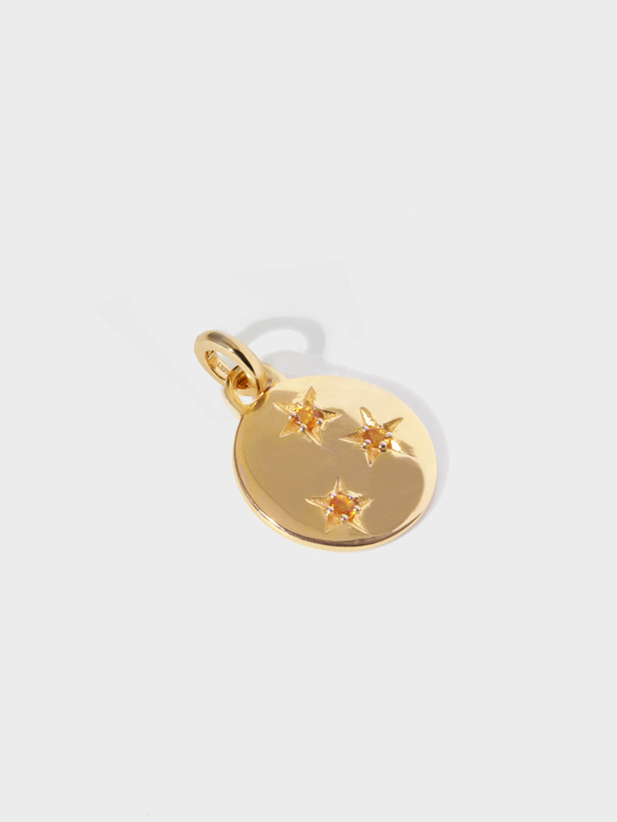 A gold circular necklace pendant set with 3 citrine gemstones in star cutouts with a large hoop at the top and clicker connector attached. Grey background with shadow.