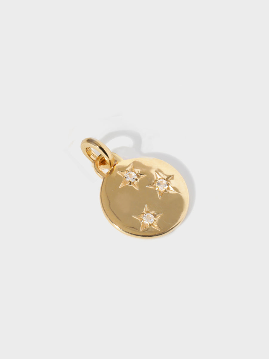 A gold circular necklace pendant set with 3 white topaz gemstones in star cutouts with a large hoop at the top and clicker connector attached. Grey background with shadow.