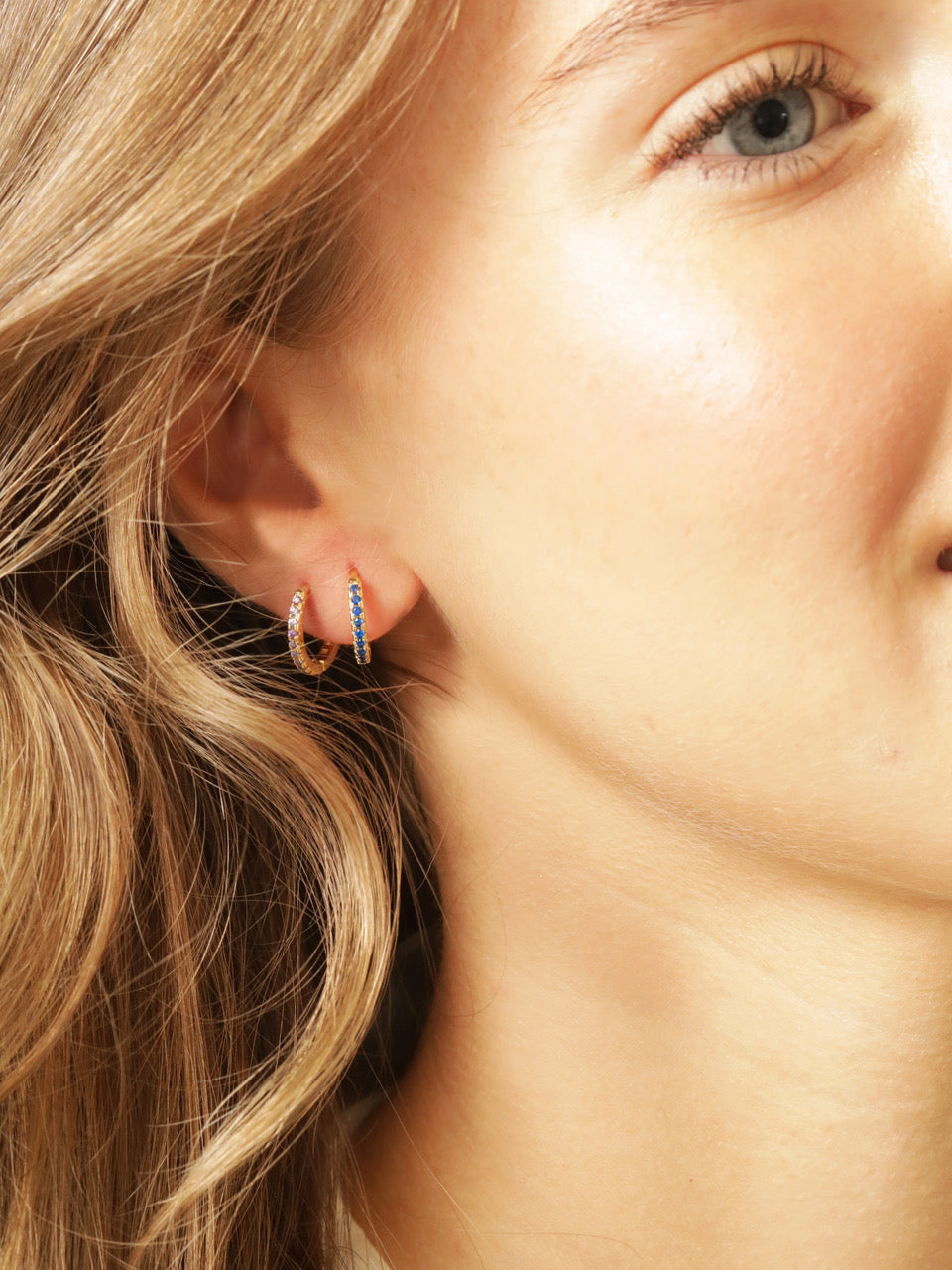 Close up of the right side of a models face wearing two huggies on her right ear. One blue tanzanite huggie and one yellow citrine huggie