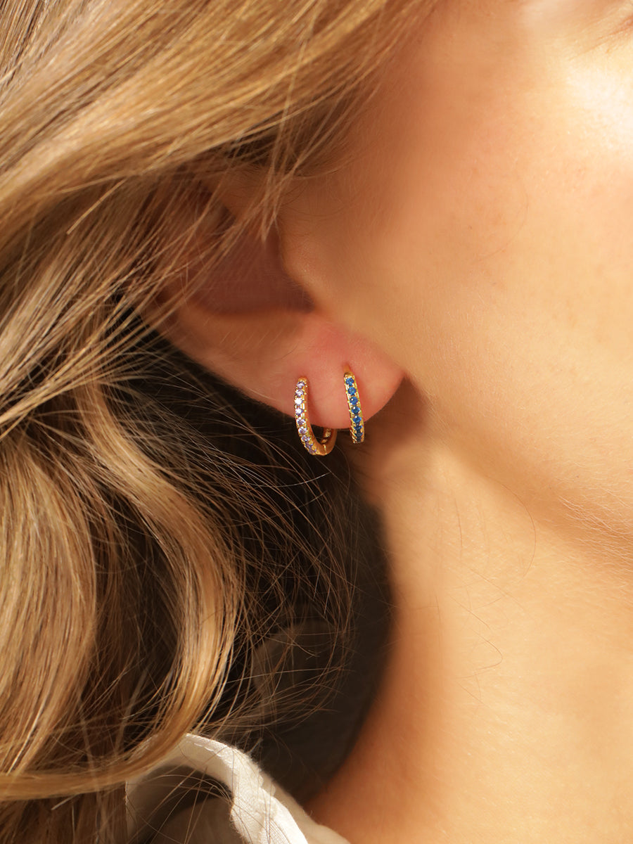 Close up of a models right ear wearing two huggies. One blue tanzanite huggie and one yellow citrine huggie