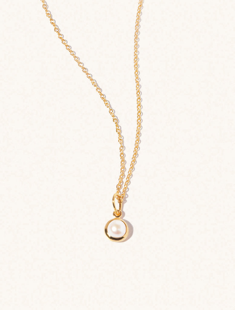 A gold delicate chain nacklace with an 8mm mother of pearl gemstone set in a round pendant. Set on an cream background with gentle shadowing.