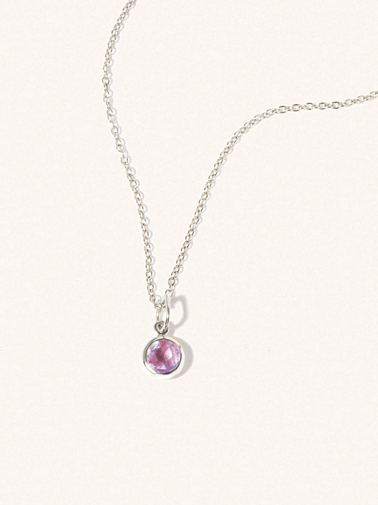 A sterling silver delicate chain nacklace with an 8mm purple Brazilian Amethyst gemstone set in a round pendant. Set on an cream background with gentle shadowing.