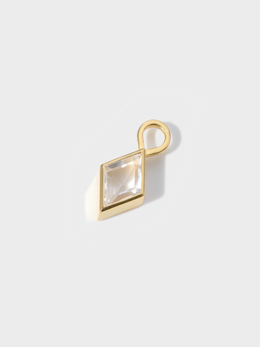 A small diamond shaped baguette shaped charm set in a gold casing with large connection hoop at the top. Grey background with shadow