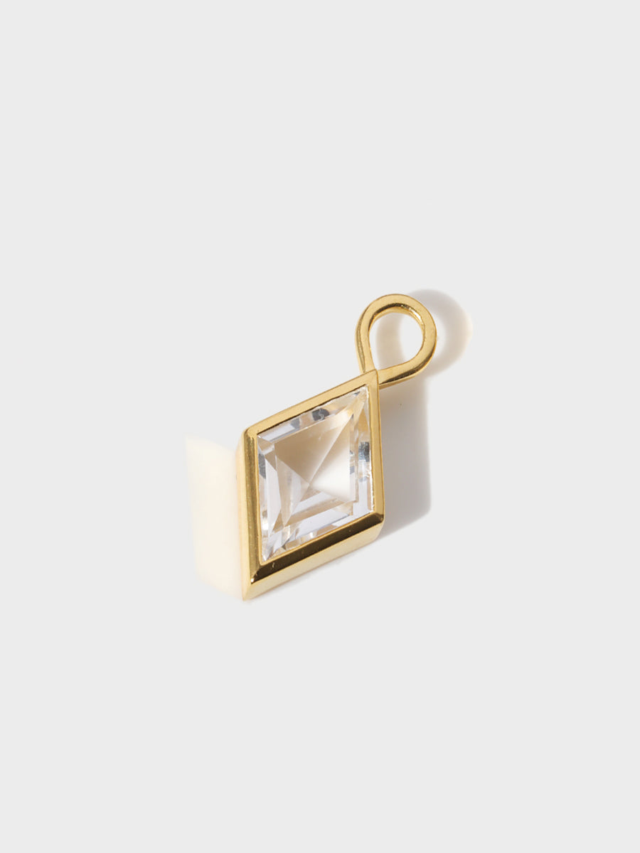 A large crystal diamond shaped charm set in a gold casing with large connection hoop at the top. Grey background with shadow