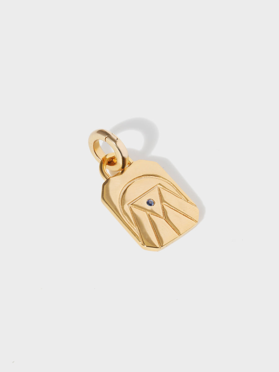 A gold water element rectangular charm with chamfered corners and a central blue sapphire and large connection hoop at the top and clicker connector attached. Grey background with shadow
