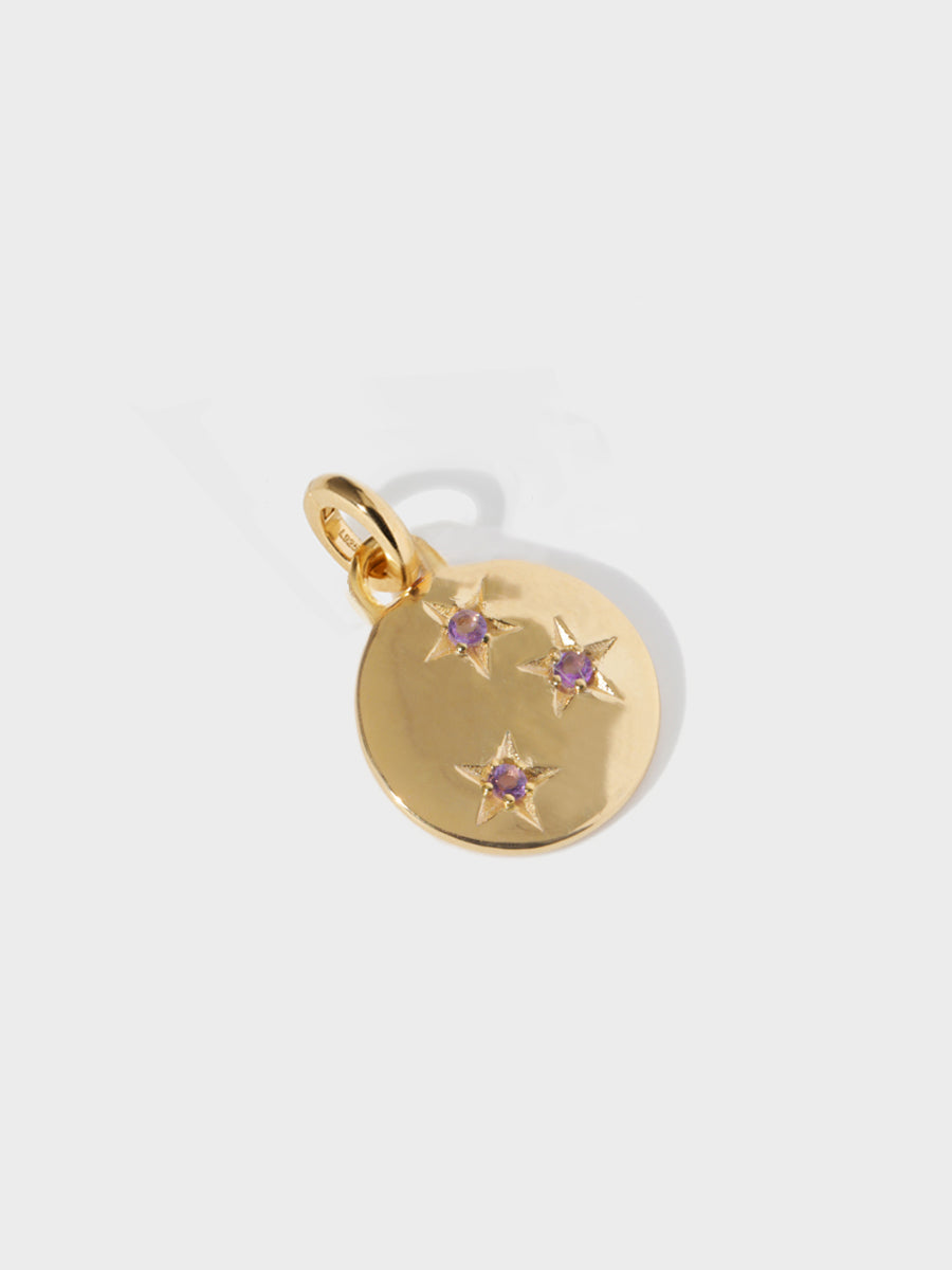A gold circular necklace pendant set with 3 Brazilian amethyst gemstones in star cutouts with a large hoop at the top and clicker connector attached. Grey background with shadow.