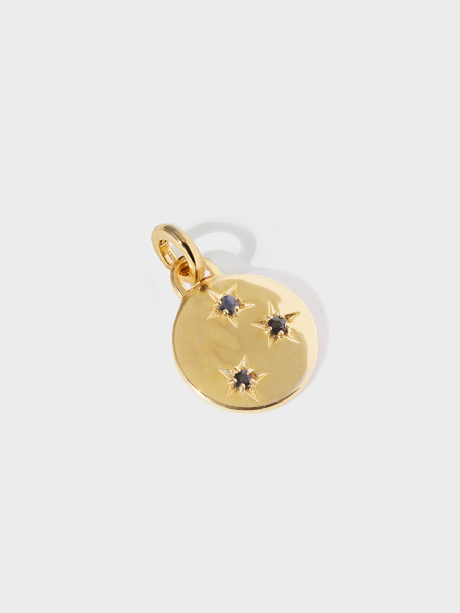 A gold circular necklace pendant set with 3 blue sapphire gemstones in star cutouts with a large hoop at the top and clicker connector attached. Grey background with shadow.
