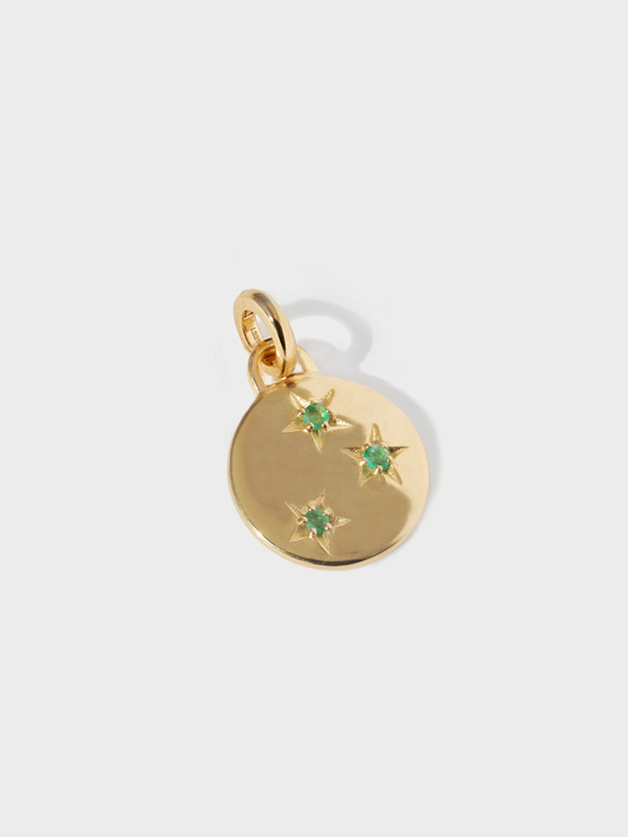 A gold circular necklace pendant set with 3 emerald gemstones in star cutouts with a large hoop at the top and clicker connector attached. Grey background with shadow.