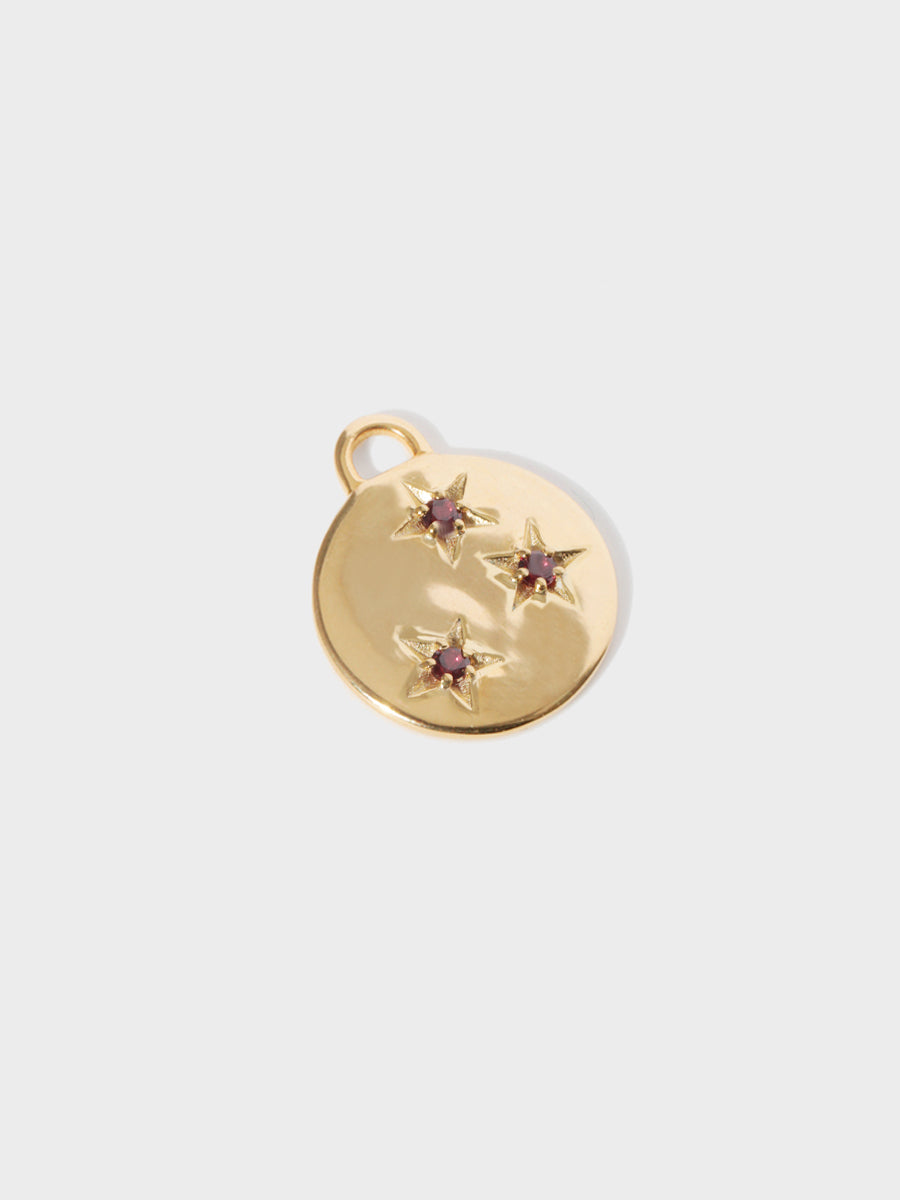 A gold circular necklace pendant set with 3 garnet gemstones in star cutouts with a large hoop at the top. Grey background with shadow.