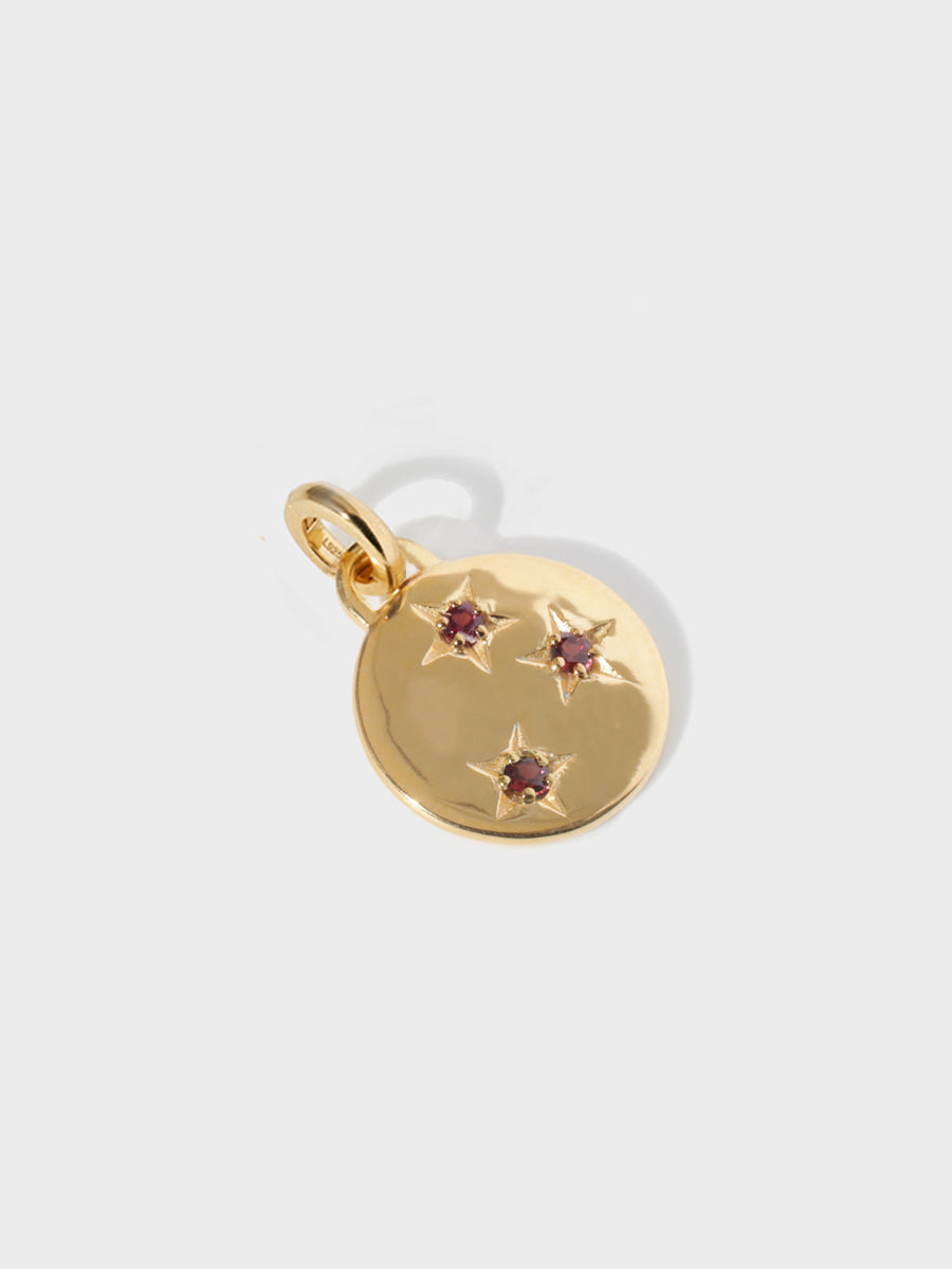 A gold circular necklace pendant set with 3 garnet gemstones in star cutouts with a large hoop at the top and clicker connector attached. Grey background with shadow.