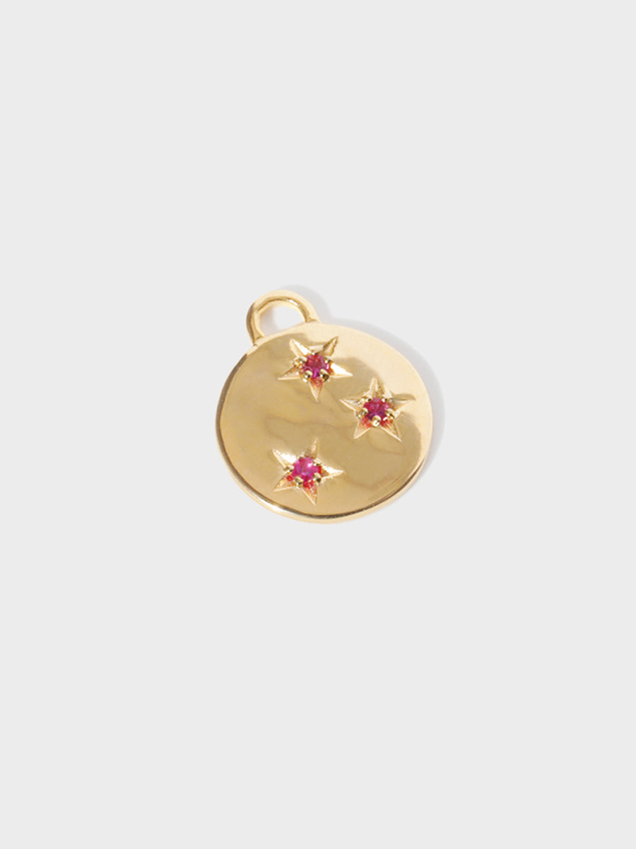 A gold circular necklace pendant set with 3 ruby gemstones in star cutouts with a large hoop at the top. Grey background with shadow.