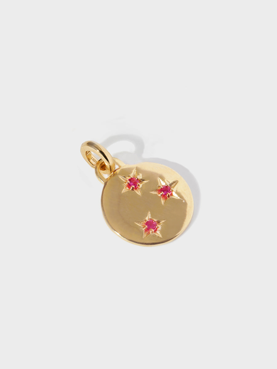 A gold circular necklace pendant set with 3 ruby gemstones in star cutouts with a large hoop at the top and clicker connector attached. Grey background with shadow.