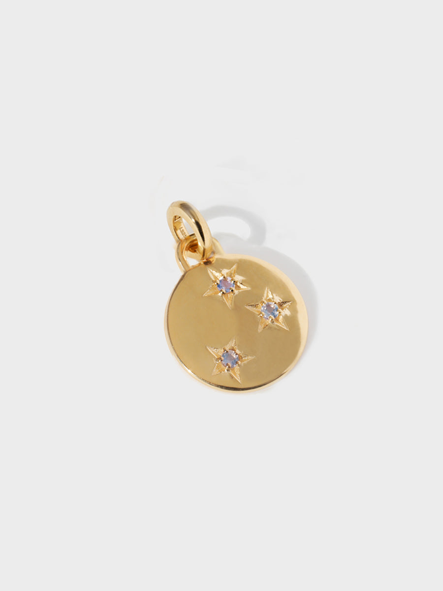A gold circular necklace pendant set with 3 tanzanite gemstones in star cutouts with a large hoop at the top and clicker connector attached. Grey background with shadow.