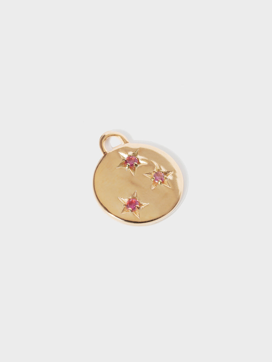 A gold circular necklace pendant set with 3 pink tourmaline gemstones in star cutouts with a large hoop at the top. Grey background with shadow.
