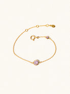 Delicate gold bracelet with two purple Brazilian Amethyst gemstones. One larger central 5mm gemstone and one smaller 2mm gemstone towards the round spring fastening. Set on a cream background with slight shadow.