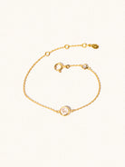 Delicate gold bracelet with two white crystal gemstones. One larger central 5mm gemstone and one smaller 2mm gemstone towards the round spring fastening. Set on a cream background with slight shadow.