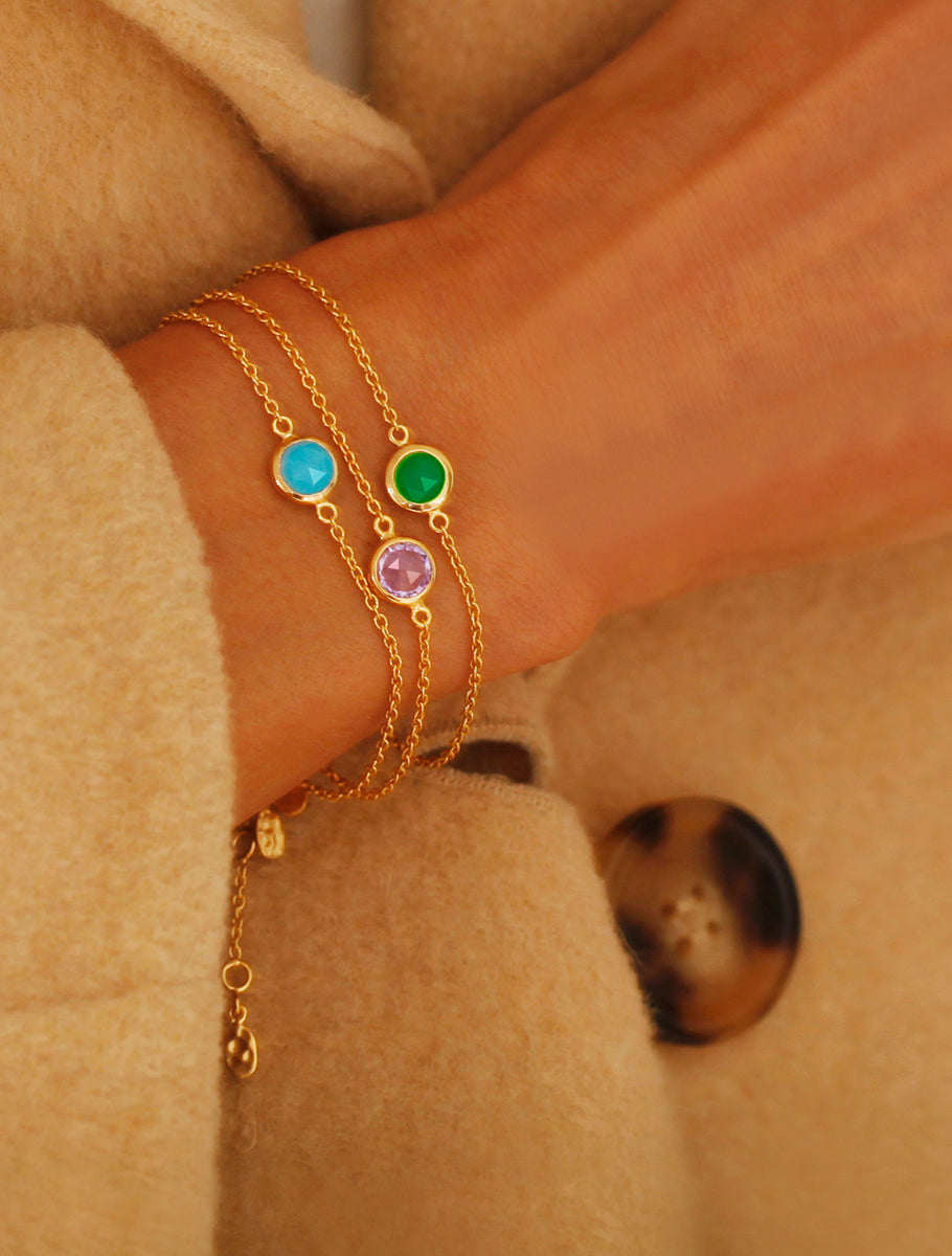 Close up of a models right wrist wearing three gold birthstone bracelets with turquoise, brazilian amethyst and emerald quartz gemstones