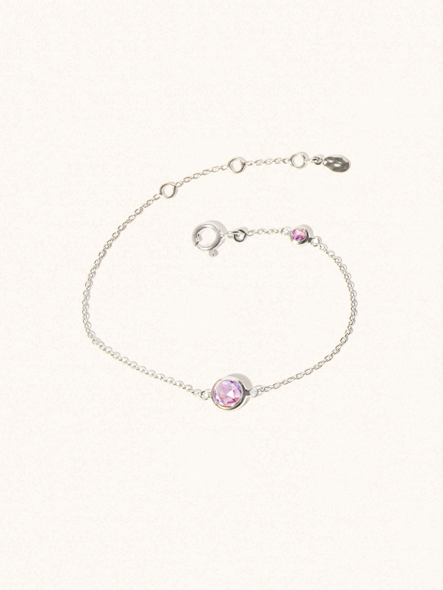 Delicate sterling silver bracelet with two purple Brazilian Amethyst gemstones. One larger central 5mm gemstone and one smaller 2mm gemstone towards the round spring fastening. Set on a cream background with slight shadow.