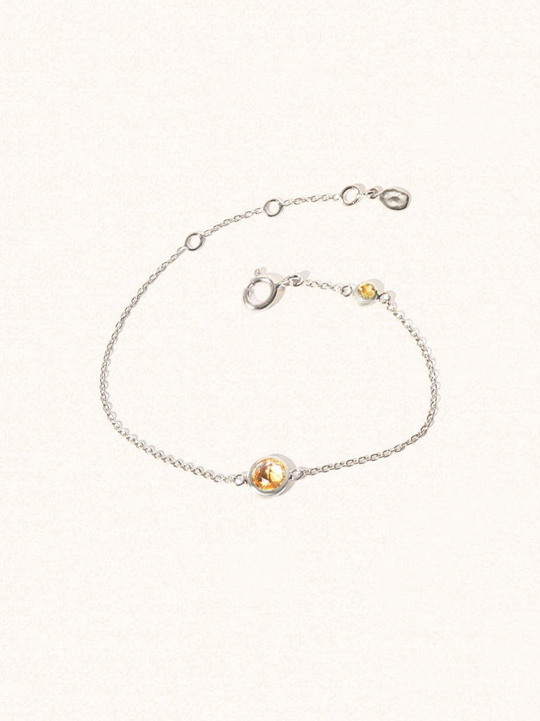 Delicate sterling silver bracelet with two yellow citrine gemstones. One larger 5mm central gemstone and one smaller 2mm gemstone towards the round spring fastening. Set on a cream background with slight shadow.