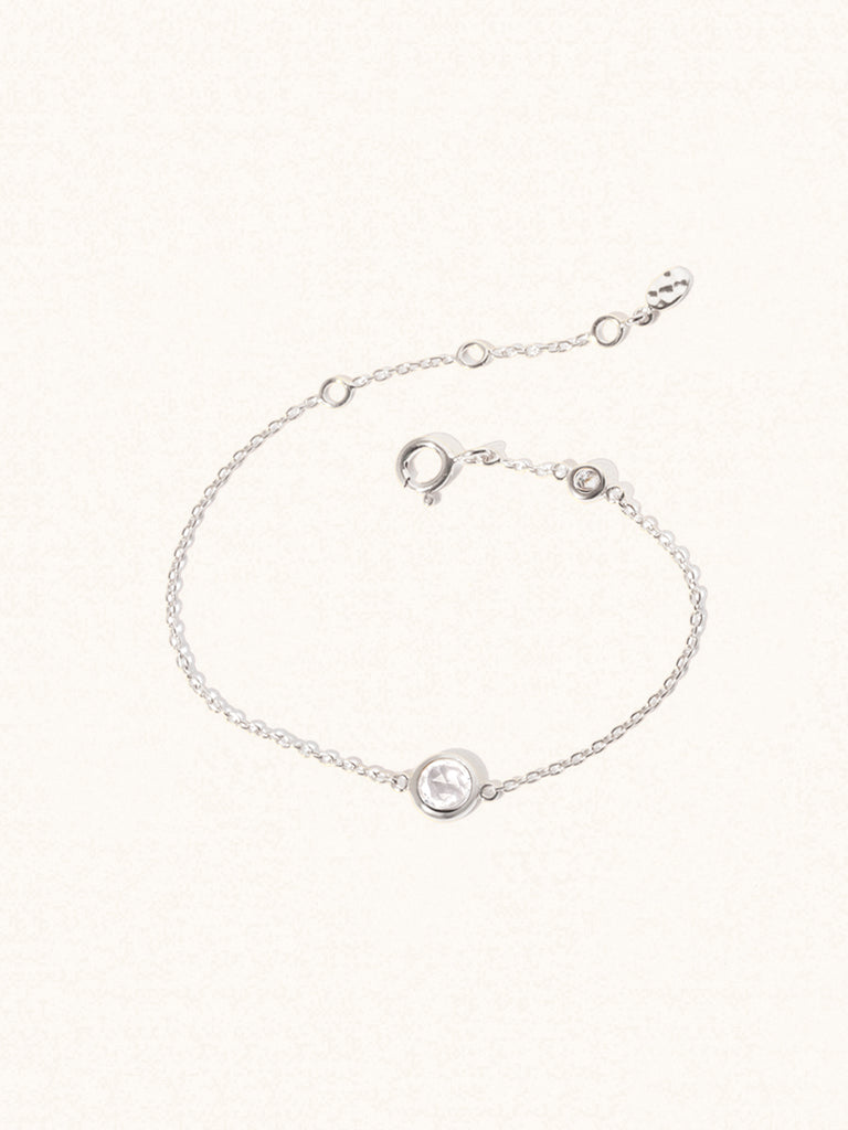 Delicate sterling silver bracelet with two white crystal gemstones. One larger central 5mm gemstone and one smaller 2mm gemstone towards the round spring fastening. Set on a cream background with slight shadow.