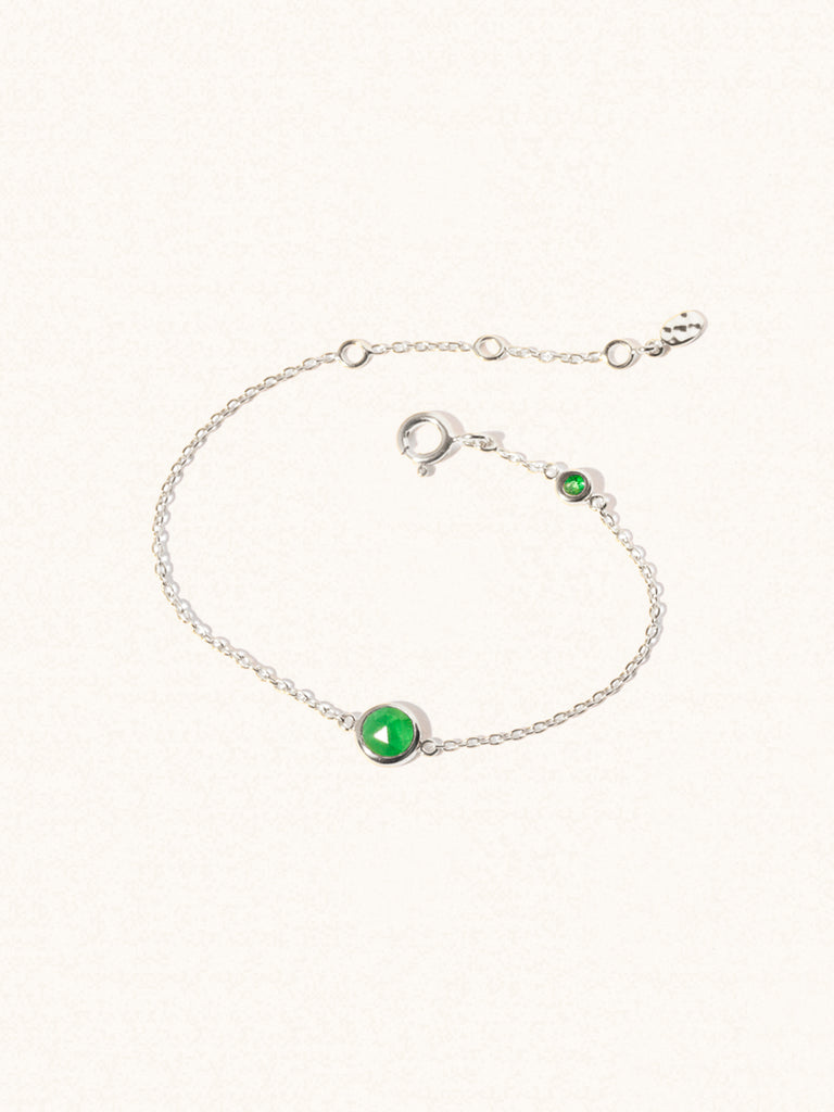 Delicate sterling silver bracelet with two emerald quartz gemstones. One larger central 5mm gemstone and one smaller 2mm gemstone towards the round spring fastening. Set on a cream background with slight shadow.