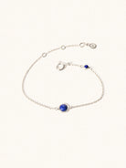 Delicate sterling silver bracelet with two blue lapiz lazuli gemstones. One larger 5mm central gemstone and one smaller 2mm gemstone towards the round spring fastening. Set on a cream background with slight shadow.