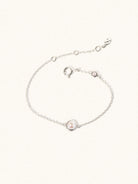 Delicate sterling silver bracelet with two mother of pearl gemstones. One larger central 5mm pearl gemstone and one smaller 2mm pearl gemstone towards the round spring fastening. Set on a cream background with slight shadow.