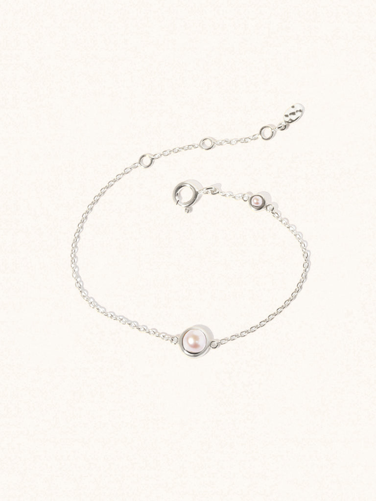 Delicate sterling silver bracelet with two mother of pearl gemstones. One larger central 5mm pearl gemstone and one smaller 2mm pearl gemstone towards the round spring fastening. Set on a cream background with slight shadow.