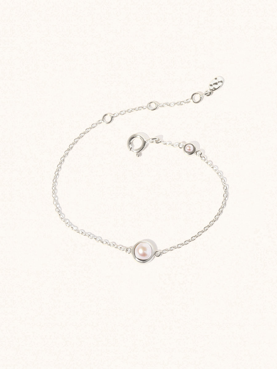 Delicate sterling silver bracelet with two mother of pearl gemstones. One larger central 5mm pearl gemstone  and one smaller 2mm pearl gemstone  towards the round spring fastening. Set on a cream background with slight shadow.