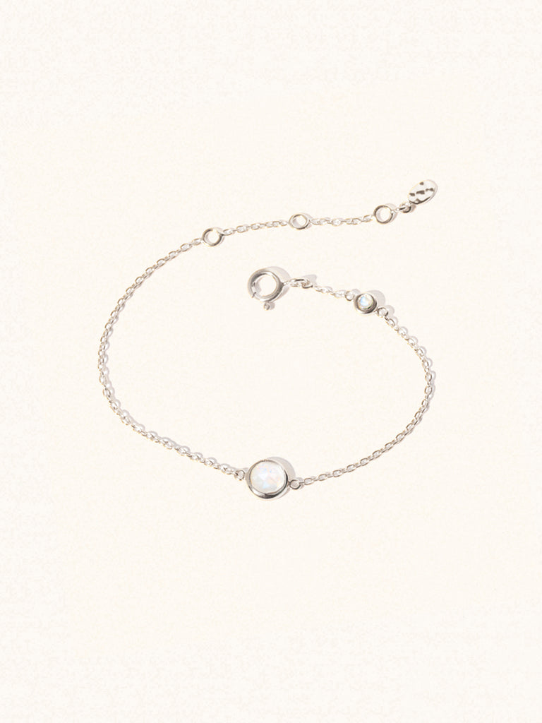 Delicate sterling silver bracelet with two iridescent moonstone gemstones. One larger central 5mm moonstone gemstone and one smaller 2mm moonstone gemstone towards the round spring fastening. Set on a cream background with slight shadow.