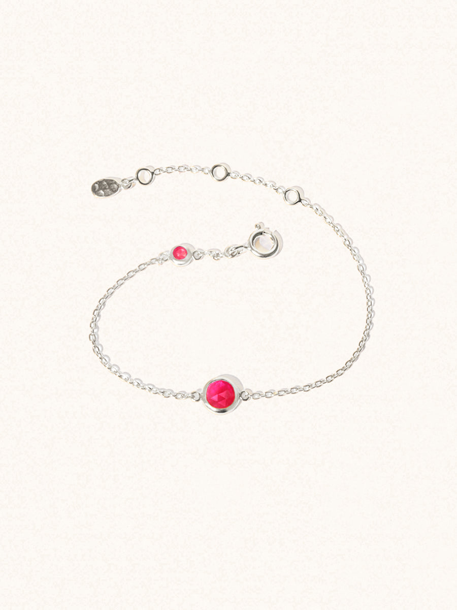 Delicate sterling silver bracelet with two ruby quartz gemstones. One larger 5mm central gemstone and one smaller 2mm gemstone towards the round spring fastening. Set on a cream background with slight shadow.