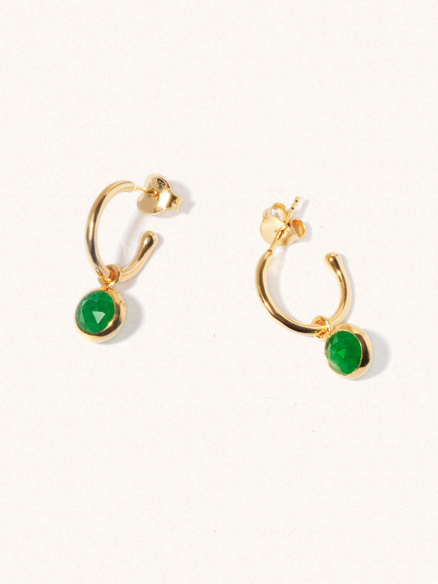 A pair of 15mm diameter gold hoop earrings each with an 8mm emerald quartz gemstone drop and butterfly fastening. Set on a cream background with gentle shadowing.