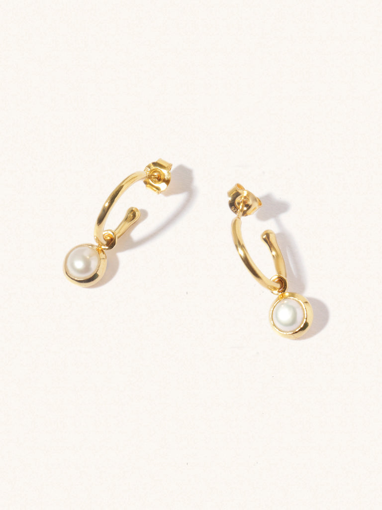 A pair of 15mm diameter gold hoop earrings each with an 8mm mother of pearl gemstone drop and butterfly fastening. Set on a cream background with gentle shadowing.