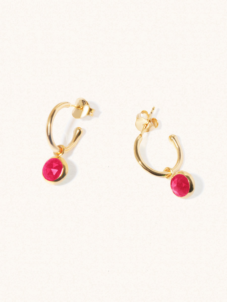 A pair of 15mm diameter gold hoop earrings each with an 8mm ruby quartz gemstone drop and butterfly fastening. Set on a cream background with gentle shadowing.