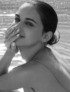 Black and white photograph of a woman looking into the camera while holding her fingers over her mouth wearing sterling silver hoop earrings