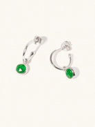 A pair of 15mm diameter sterling silver hoop earrings each with an 8mm emerald quartz gemstone drop and butterfly fastening. Set on a cream background with gentle shadowing.