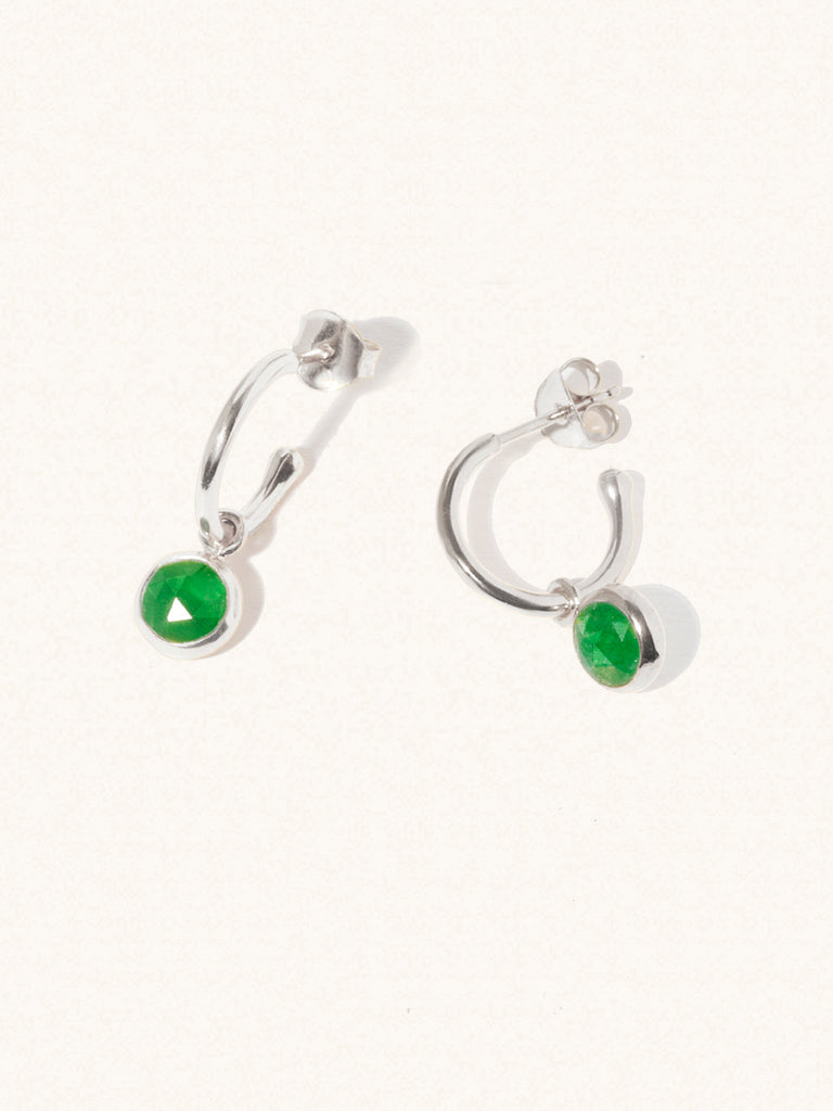 A pair of 15mm diameter sterling silver hoop earrings each with an 8mm emerald quartz gemstone drop and butterfly fastening. Set on a cream background with gentle shadowing.