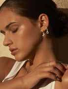 Left side face of a brunette model looking down with her eyes closed wearing a sterling silver hoop earring with a blue lapis lazuli gemstone drop and another sterling silver hoop earring with a letter X drop