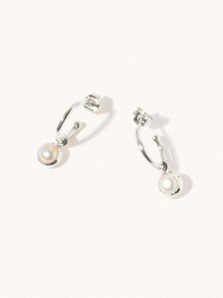 A pair of 15mm diameter sterling silver hoop earrings each with an 8mm mother of pearl gemstone drop and butterfly fastening. Set on a cream background with gentle shadowing.