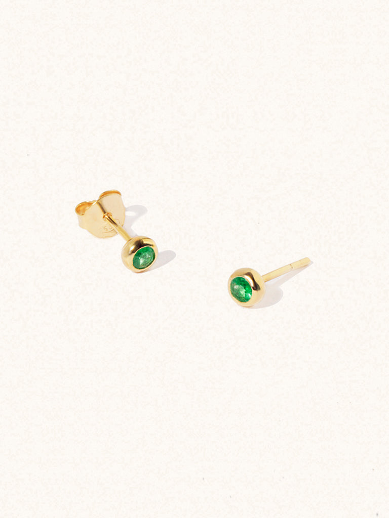 A pair of gold small stud earrings with a 3mm emerald quartz gemstone in a 4mm setting and butterfly fastening. Set on a cream background with gentle shadowing.