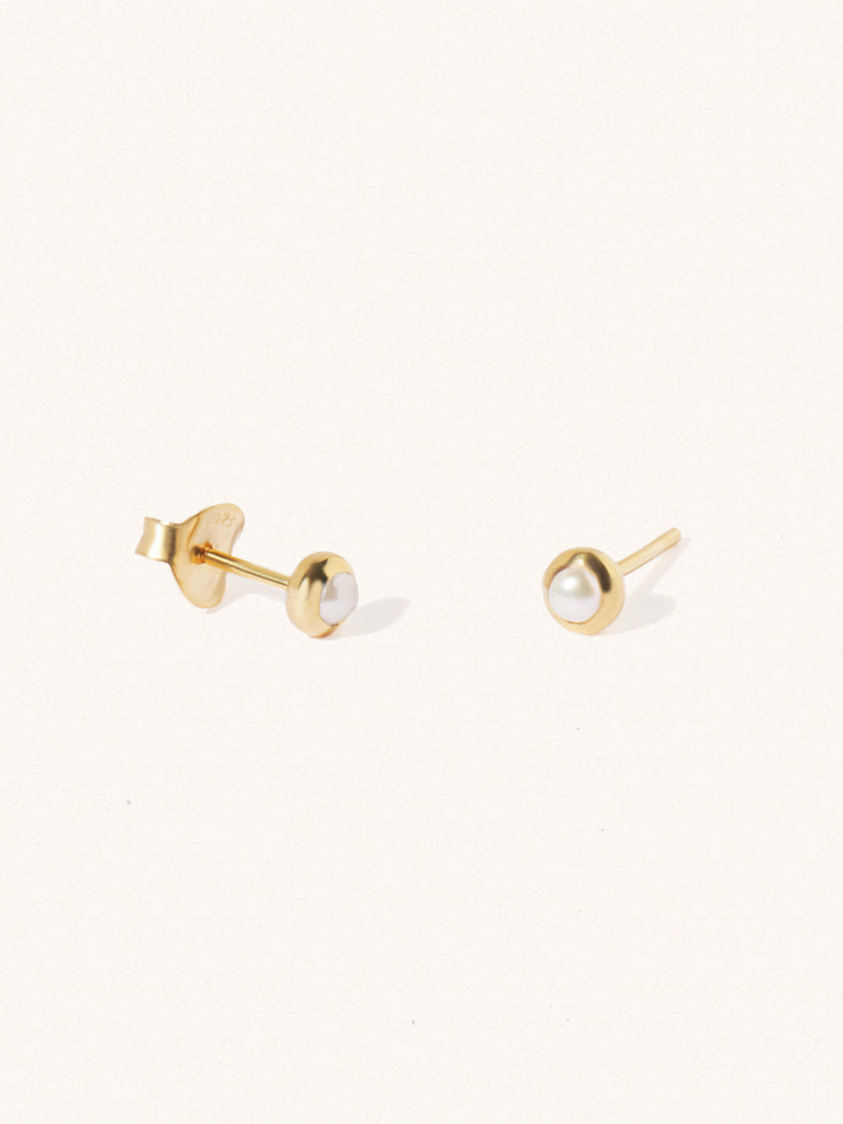 A pair of gold small stud earrings with a 3mm mother of pearl gemstone in a 4mm setting and butterfly fastening. Set on a cream background with gentle shadowing.