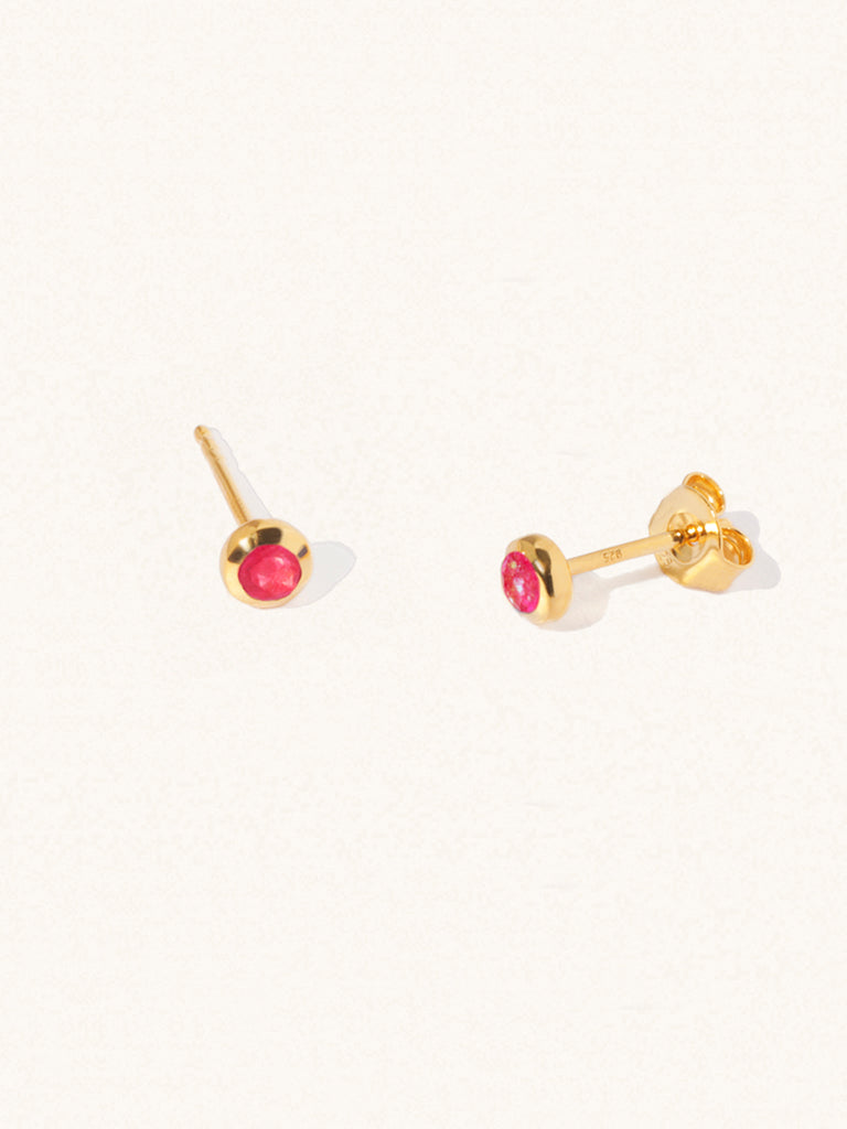 A pair of gold small stud earrings with a 3mm ruby quartz gemstone in a 4mm setting and butterfly fastening. Set on a cream background with gentle shadowing.