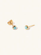 A pair of gold small stud earrings with a 3mm turquoise gemstone in a 4mm setting and butterfly fastening. Set on a cream background with gentle shadowing.