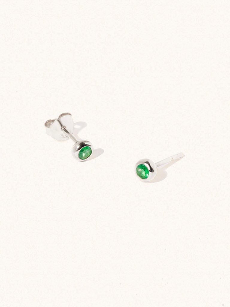 A pair of sterling silver small stud earrings with a 3mm emerald quartz gemstone in a 4mm setting and butterfly fastening. Set on a cream background with gentle shadowing.