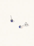 A pair of sterling silver small stud earrings with a 3mm blue lapis lazuli gemstone in a 4mm setting and butterfly fastening. Set on a cream background with gentle shadowing.