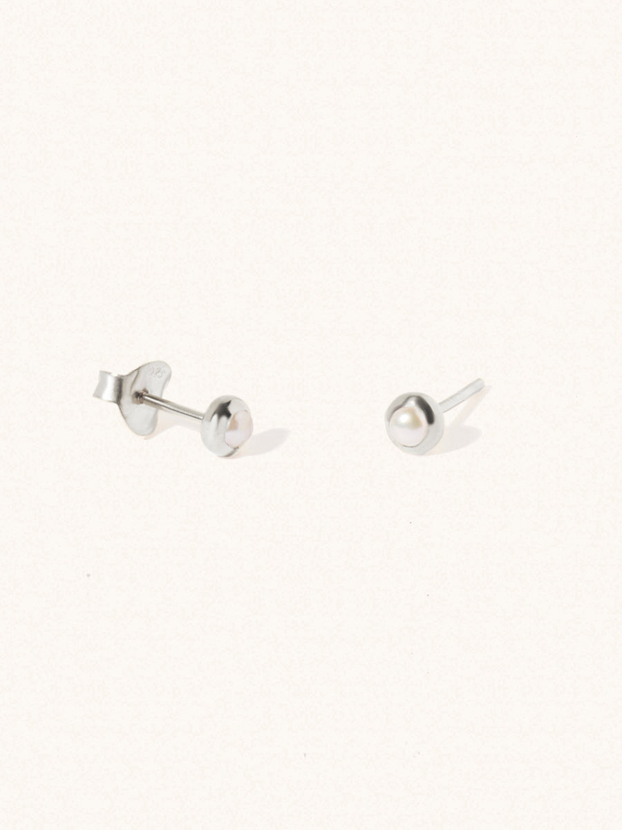 A pair of sterling silver small stud earrings with a 3mm mother of pearl gemstone in a 4mm setting and butterfly fastening. Set on a cream background with gentle shadowing.